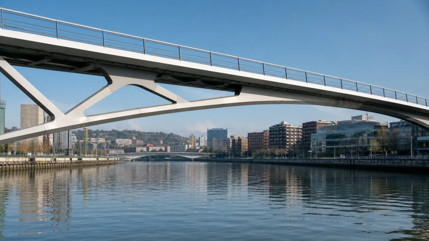 Estructura blanca de un puente de Bilbao cruzando el Nervión, con otro puente al fondo y reflejos de la ribera sobre el agua.