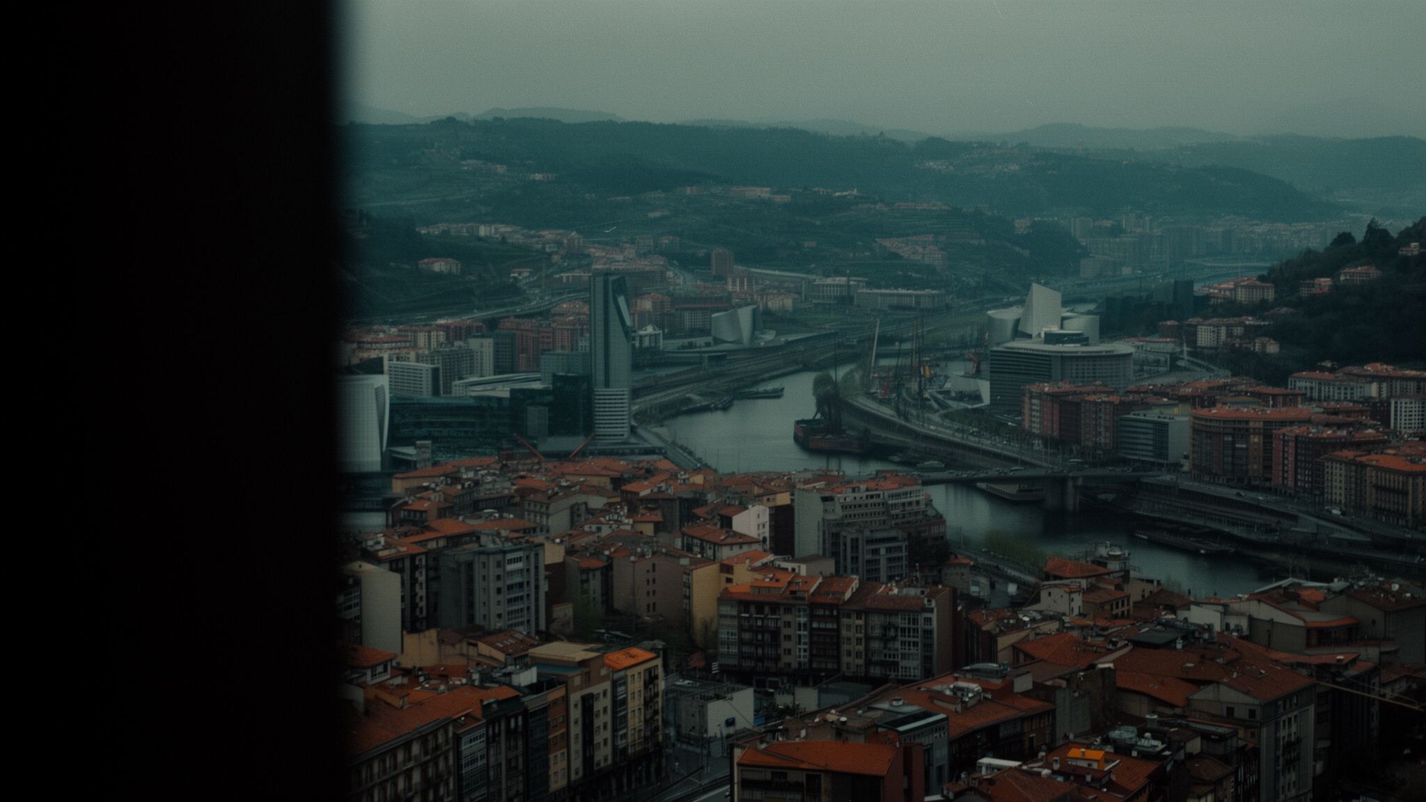 Vista nocturna del río Nervión en Bilbao con reflejos cálidos sobre el agua y una silueta urbana iluminada al fondo.